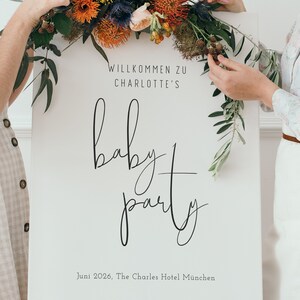 Puede incluir: Un cartel blanco con caligraf&iacute;a negra que dice "Willkommen zu Charlotte's baby party" y "Juni 2026, The Charles Hotel Munchen". El cartel est&aacute; decorado con un arreglo floral de flores rojas, naranjas, amarillas y azules.