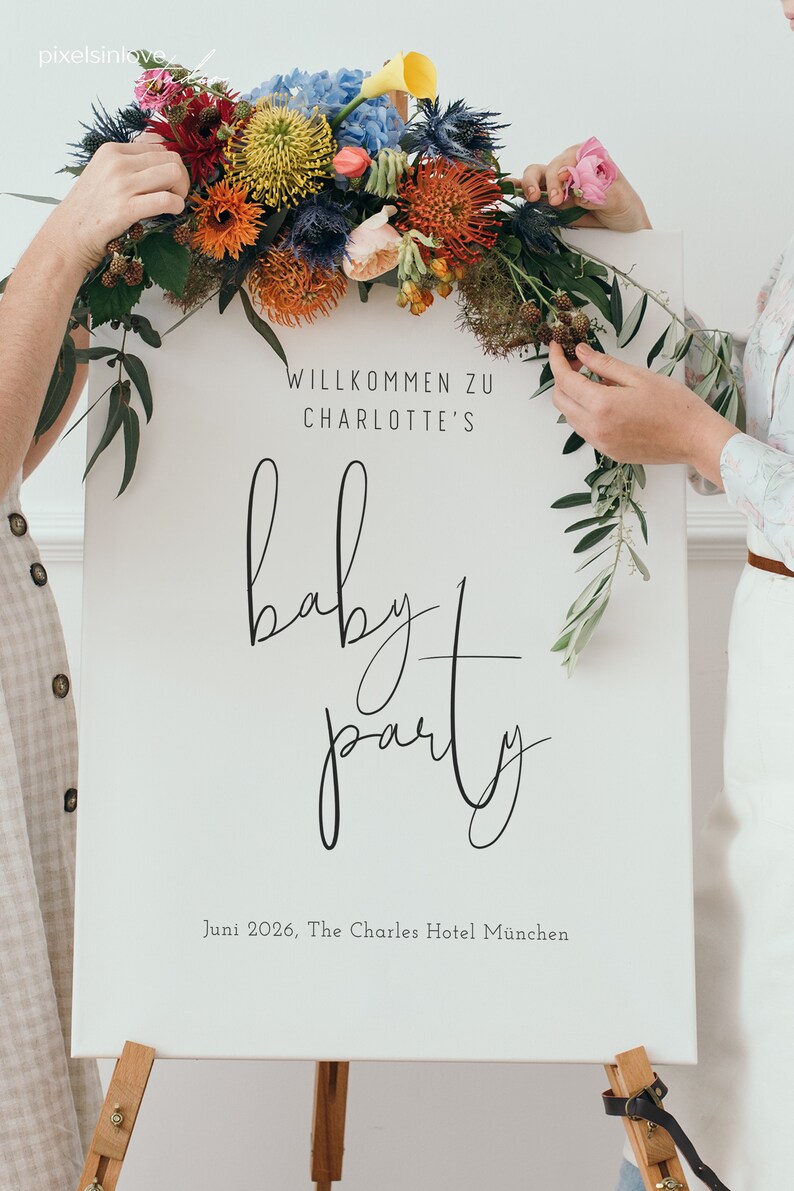 Puede incluir: Un cartel blanco con caligraf&iacute;a negra que dice "Willkommen zu Charlotte's baby party" y "Juni 2026, The Charles Hotel Munchen". El cartel est&aacute; decorado con un arreglo floral de flores rojas, naranjas, amarillas y azules.