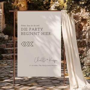 以下が含まれることがあります： 「Schon, dass ihr da seid. DIE PARTY BEGINNT HIER.」という黒い文字が書かれた白い看板。テキストの下には黒い山形の記号があり、その下には筆記体で「Charlitte + Kasper」という文字が書かれている。さらにその下には「17. Juli 2026 | The Charles Hotel München」という文字が書かれている。