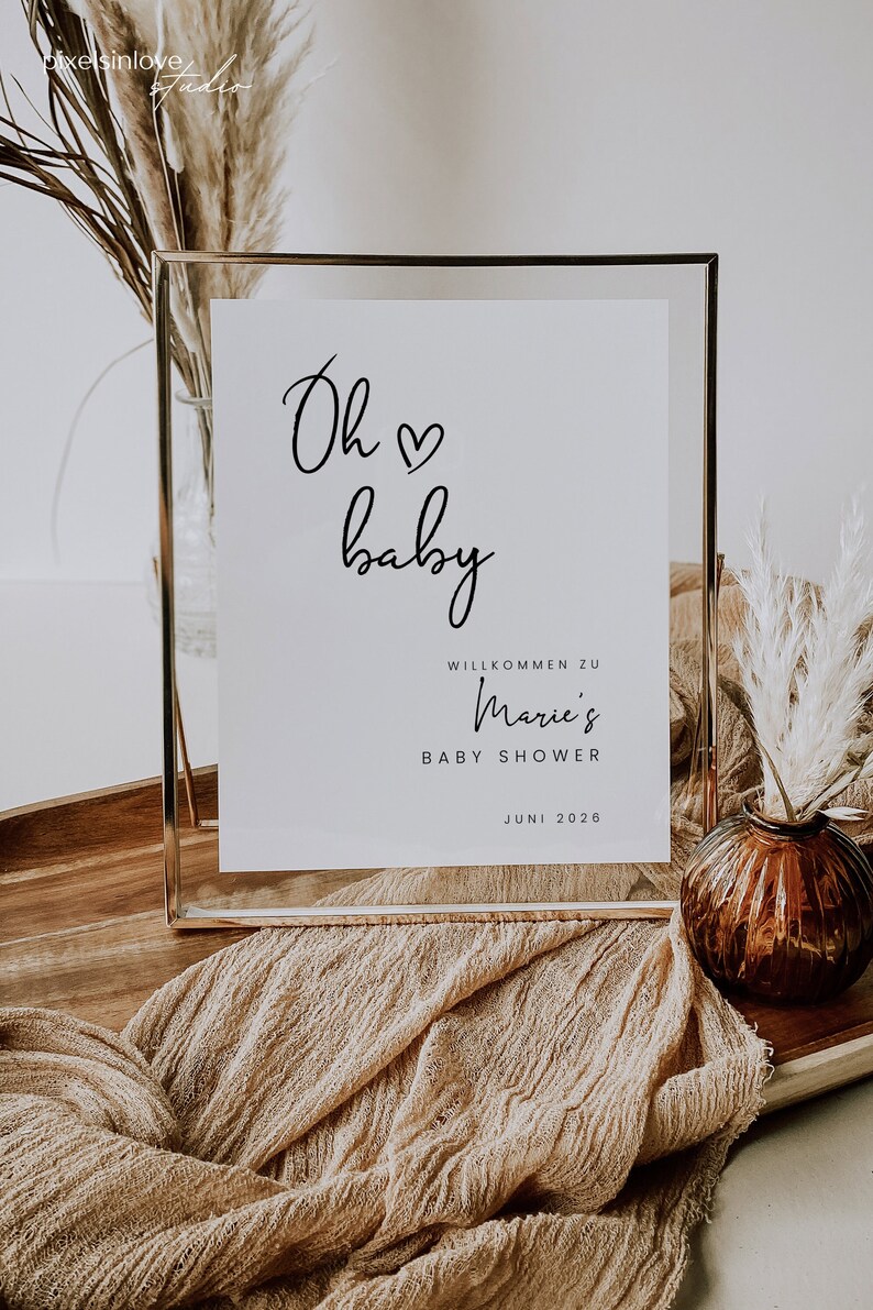 Puede incluir: Un cartel con marco dorado con el texto "Oh baby" en cursiva con un s&iacute;mbolo de coraz&oacute;n. El cartel tambi&eacute;n incluye el texto "Willkommen zu Marie's Baby Shower Juni 2026".
