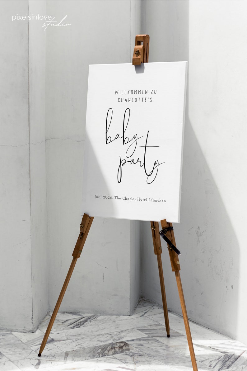 Puede incluir: Un cartel blanco con texto negro en un caballete de madera. El cartel dice "Willkommen zu Charlotte's baby party Juni 2026, The Charles Hotel Munchen".