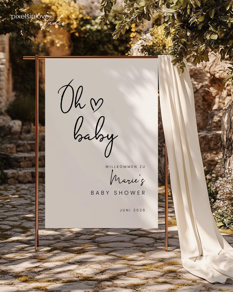 Puede incluir: Un cartel blanco con texto negro que dice "Oh baby" con un s&iacute;mbolo de coraz&oacute;n. El cartel tambi&eacute;n dice "Willkommen zu Marie's Baby Shower Juni 2026". El cartel est&aacute; apoyado en un soporte dorado frente a una cortina blanca.