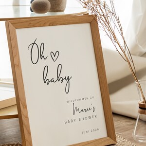 Puede incluir: Un cartel enmarcado con el texto "Oh baby" en letra cursiva con un s&iacute;mbolo de coraz&oacute;n. El cartel tambi&eacute;n incluye el texto "Willkommen zu Marie's Baby Shower Juni 2026".