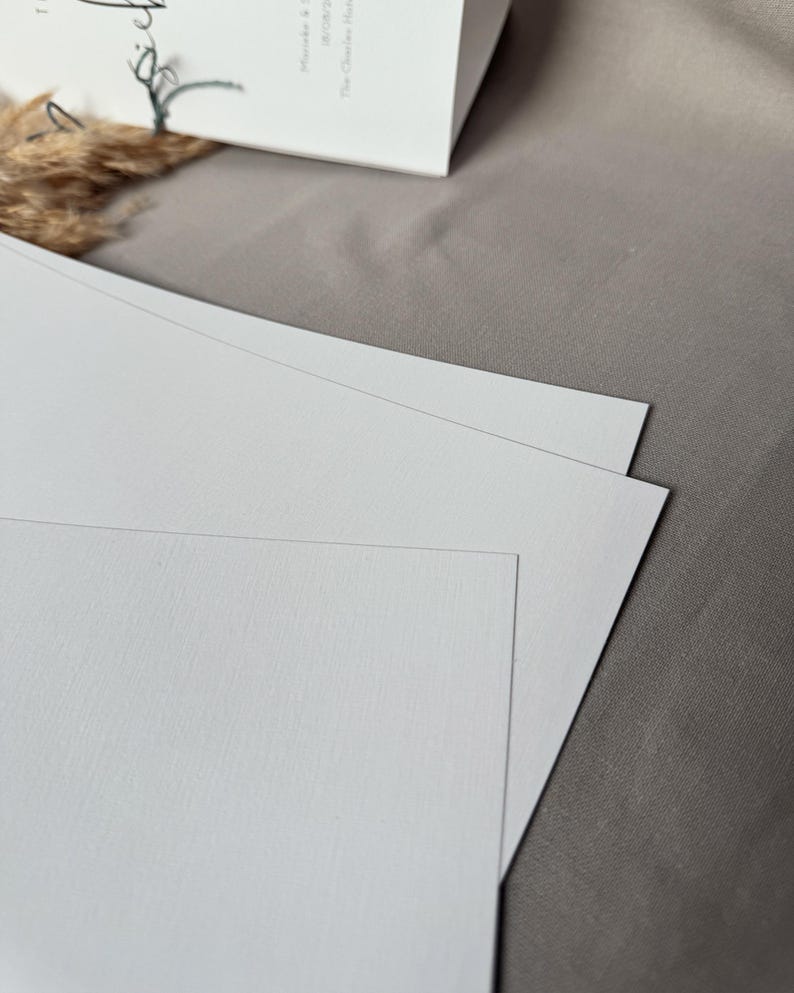 May include: Three white blank cards stacked on top of each other on a light brown surface.
