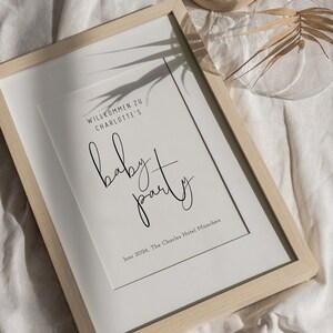 Puede incluir: Un cartel enmarcado blanco con texto negro que dice "Willkommen zu Charlotte's baby party" y "Juni 2026, The Charles Hotel M&uuml;nchen".