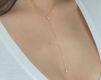 May include: A delicate gold chain necklace with two small, clear gemstones. The necklace is long and hangs down to the chest.