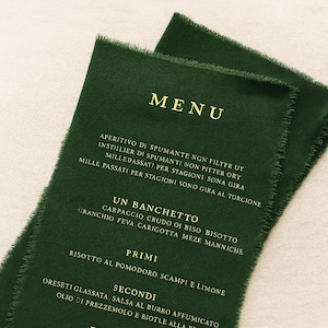 Könnte beinhalten: Eine dunkelwaldgrüne, rechteckige Menükarte mit ausgefransten, rohen Kanten. Der Text ist in einer goldenen Serifenschrift gedruckt und enthält die Überschriften MENU, UN BANCHETTO, PRIMI, SECONDI und DOLCEZZE sowie verschiedene Speisen in Italienisch.