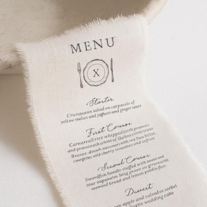 以下が含まれることがあります： 縁がほつれたオフホワイトのリネンのメニューカード。メニューにはフォークとナイフのグラフィックがあり、甲殻類のサラダやメカジキの束などの料理を含む、コース料理が記載されています。