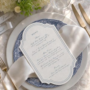 May include: A die-cut menu card with a decorative scalloped edge and blue border, featuring printed text listing starters, main courses, and desserts. The menu is placed on a white plate with a blue floral pattern, accompanied by a white napkin.