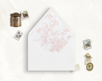 May include: A white envelope with a pink floral pattern lining the inside flap. The envelope is lying flat on a white surface with several vintage postage stamps scattered around it.