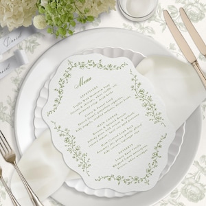Op de afbeelding: Een gestanst papieren menukaart met een geschulpte rand en een groene bloemenrand, met de tekst Menu, Appetisers, Main Course en Desserts. Het menu bevat gerechten zoals truffel-wilde paddenstoelensoep, ricotta-spinazie-ravioli en citroen-basilicum-vanille.