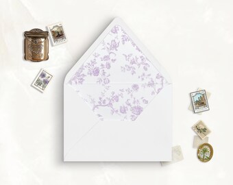 May include: A white envelope with a pointed flap featuring a light purple floral pattern on the interior lining. The envelope is surrounded by several small postage stamps and a miniature bronze-colored mailbox ornament on a plain white surface.