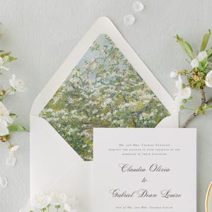 May include: Elegant wedding stationery set. A white envelope with a floral artwork lining, a matching invitation card, and delicate white blossom branches. The invitation reads "Claudia Olivia to Gabriel Dean Louise."