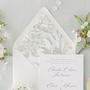 Op de afbeelding: Een witte huwelijksuitnodiging met een bloemenpatroon op de envelop. De uitnodiging luidt: "Mr. en Mrs. Charles Fontaine verzoeken u de eer te bewijzen aanwezig te zijn bij het huwelijk van hun dochter Claudia Olivia Fontaine met Elias Moreau."