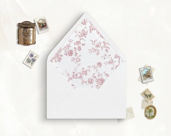 May include: A white envelope with an open triangular flap featuring a dusty rose floral pattern on the interior lining. The envelope is surrounded by several small postage stamps and a miniature bronze-colored metal mailbox ornament.