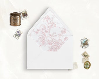 May include: A white envelope with an open flap featuring a soft pink floral pattern on the interior lining. The envelope is surrounded by several small postage stamps and a miniature metallic mailbox ornament with a detailed embossed design.