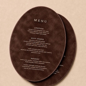 May include: Two oval-shaped dark brown menus with a suede-like texture. The top menu features the word MENU in white, followed by sections for APPETISER, MAIN COURSE, and DESSERT, listing various food items including truffle soup and tiramisu.