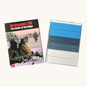 Può includere: Una scatola di gioco da tavolo intitolata "Ardennes '44 The Battle of the Bulge" con un'illustrazione di una scena di guerra. Accanto, una pila di cinque vassoi portaoggetti multicolori nelle tonalità del blu, grigio e bianco.