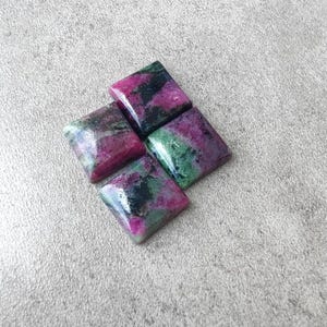 Peut inclure: Quatre pierres précieuses polies de forme carrée disposées en losange. Chaque pierre présente un mélange tacheté de magenta profond, de vert foncé et d'inclusions minérales noires avec une surface lisse et réfléchissante et des bords biseautés.