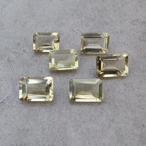 Peut inclure: Six pierres précieuses rectangulaires jaune clair sont disposées sur une surface grise. Les gemmes ont une coupe rectangulaire aux coins légèrement arrondis et sont translucides. L'ensemble suggère une collection de pierres précieuses en vrac.