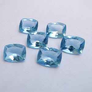 May include: Six light blue, square-cut gemstones are displayed against a white background. The gems have a faceted surface, reflecting light. The gems are a pale, sky blue colour. These gemstones are suitable for jewellery making.