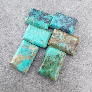 May include: Six rectangular turquoise gemstones with brown and dark blue veining. The stones are arranged on a grey surface. The turquoise colour varies from light to dark, with some stones showing more brown or blue patterns.