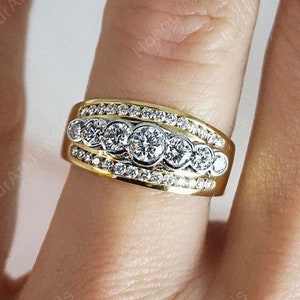 May include: A gold band ring with a row of five round diamonds set in a white metal band. The ring is surrounded by smaller diamonds.
