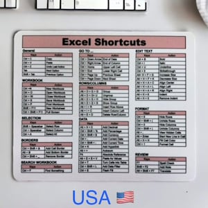 May include: A rectangular mousepad with the text "Excel Shortcuts" in a pink and white design. The mousepad lists keyboard shortcuts for various Excel functions, including general, workbook, and data operations. The word "USA" is at the bottom with a small American flag.