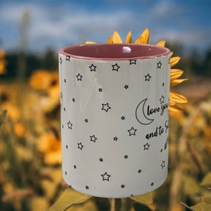 May include: White ceramic mug with a pink rim and a black and white design of stars and a crescent moon. The text on the mug reads "Love you to the moon and to the stars".