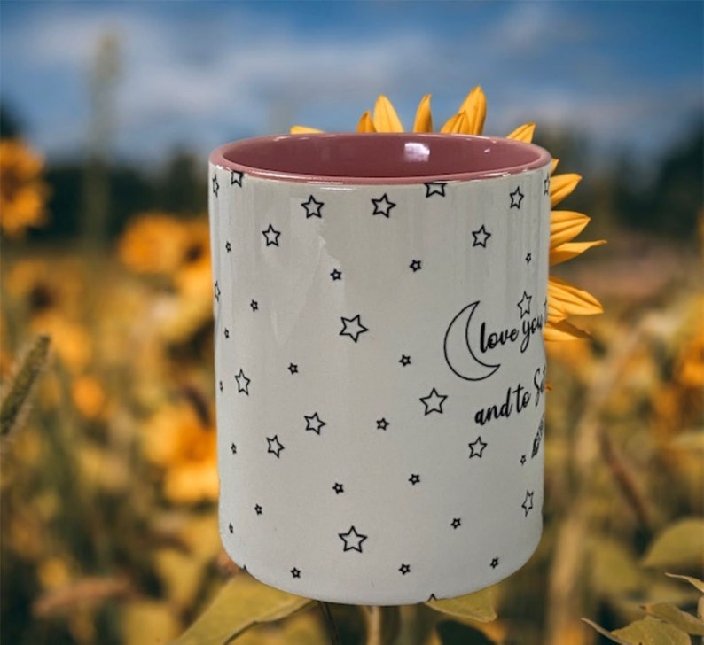 May include: White ceramic mug with a pink rim and a black and white design of stars and a crescent moon. The text on the mug reads "Love you to the moon and to the stars".