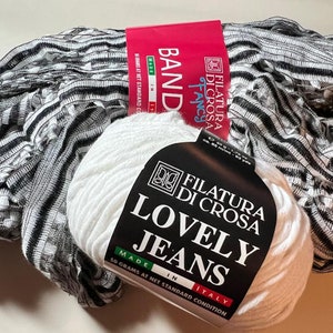 Pu&ograve; includere: Un gomitolo di lana bianco con un'etichetta nera che recita "Filatura Di Crosa Lovely Jeans Made in Italy 50 grammi in condizione standard netta". La lana &egrave; accanto a un tessuto a righe bianche e nere.