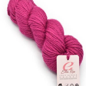 Peut inclure: Une pelote de fil d'alpaga rose étiquetée "Ella Rae Cozy Alpaca Chunky" avec un mélange d'alpaga bébé lavable en machine. L'étiquette comprend également les certifications "Oeko-Tex Standard 100", "GOTS" et "Superwash".