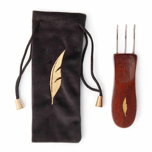 May include: A dark brown wooden hair tool with three metal prongs, next to a black velvet pouch with a gold feather design. The pouch has a drawstring closure with gold-colored metal tips. The hair tool also has a gold feather design.
