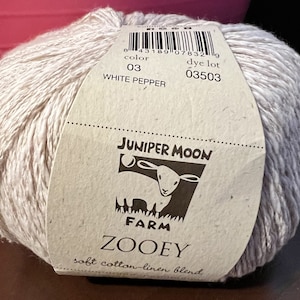 Op de afbeelding: Een bol wit en grijs garen met het label "Juniper Moon Farm Zooey soft cotton-linen blend" in de kleur "White Pepper" en de verflotnummer 03503.