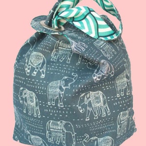 May include: A teal blue reusable shopping bag with a white elephant print. The bag has a green and white striped handle.