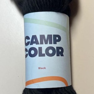 May include: A skein of black yarn with a label that reads "CAMP COLOR" and "Black".