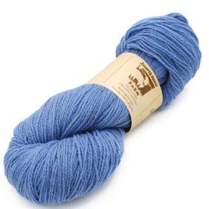 May include: A skein of Juniper Moon Farm organic merino yarn in a light blue color. The yarn is wrapped with a tan paper label that has the brand name and logo printed on it. The yarn is tightly wound and ready for knitting or crocheting.