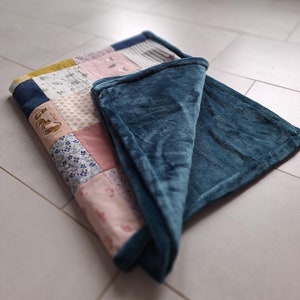 Peut inclure: Une courtepointe en patchwork avec une variété de motifs floraux et géométriques dans des tons de rose, bleu et jaune. La courtepointe est pliée en deux et surmontée d'une couverture en polaire bleu foncé.