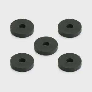 May include: Five black, circular washers with a central hole are arranged against a light gray background. Each washer is approximately 1.5 inches in diameter and 0.25 inches thick. The washers are evenly spaced and appear to be made of a solid material.