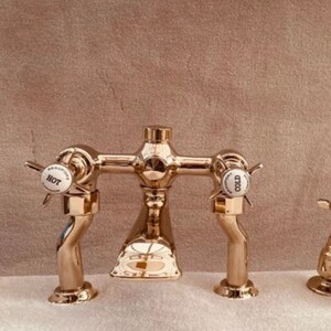 May include: A gold-colored bathroom faucet with a classic design. The faucet has two handles labeled "HOT" and "COLD" and a central spout. The finish is shiny and reflective, suggesting a high-end fixture.