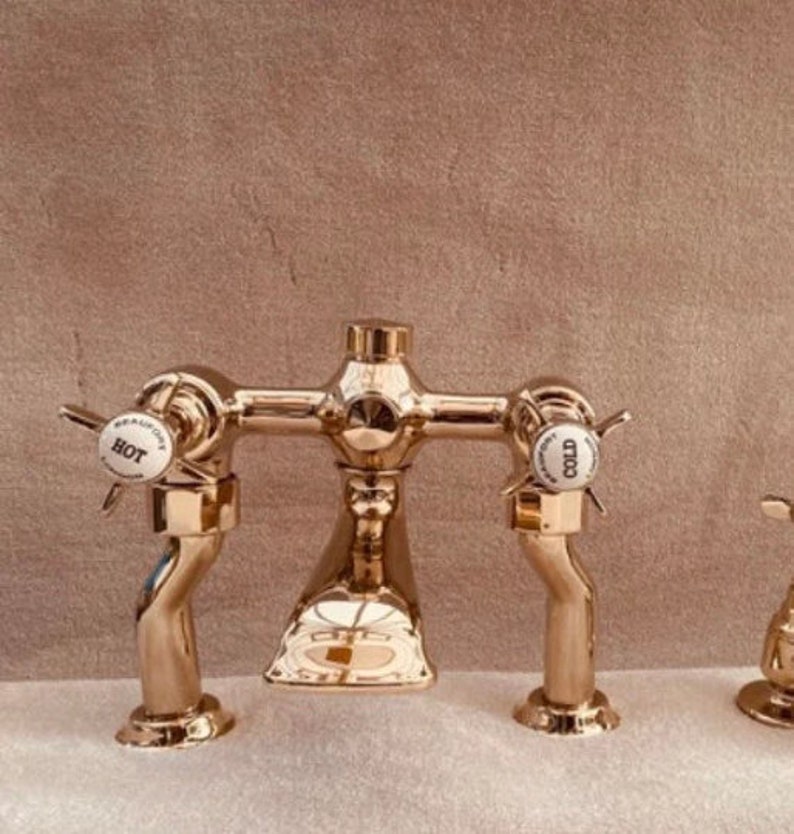 May include: A gold-colored bathroom faucet with a classic design. The faucet has two handles labeled "HOT" and "COLD" and a central spout. The finish is shiny and reflective, suggesting a high-end fixture.