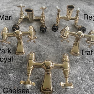 May include: Several gold-colored bathroom faucets are displayed, each with a unique design. The faucets have cross-shaped handles and are labeled with names like "Marl," "Regent," and "Chelsea." The image is taken from a top-down perspective.
