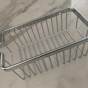 May include: A chrome-plated wire bathroom shower caddy with a rectangular shape. The caddy has a smooth, shiny finish and is designed to hold toiletries.