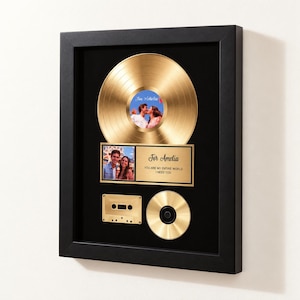 May include: A black framed wall display featuring a gold vinyl record with a photo of a couple in the centre. Below is a plaque with a photo of the same couple, the text For Amelia, YOU ARE MY ENTIRE WORLD I NEED YOU, a gold cassette, and a gold CD.