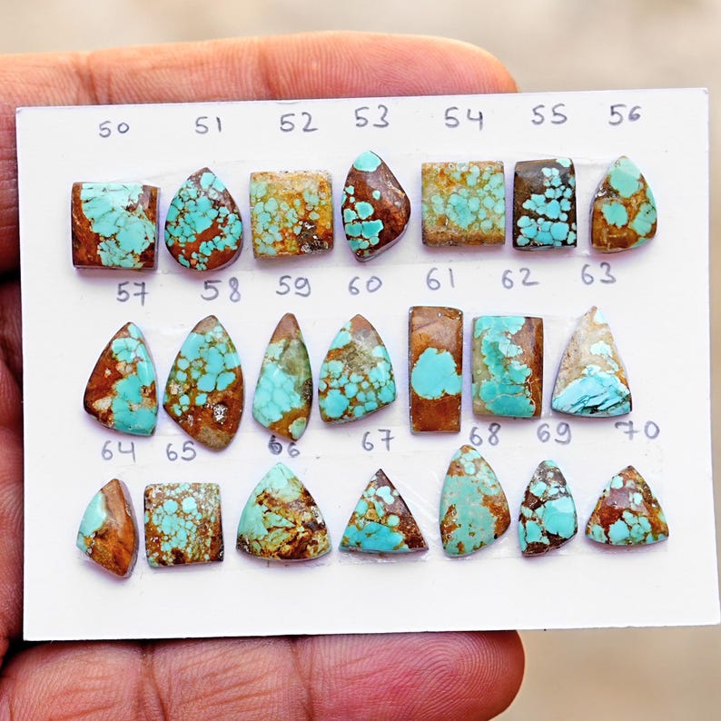 Puede incluir: Una tarjeta de presentaci&oacute;n blanca con veintiuna piedras preciosas de turquesa dispuestas en tres filas. Cada piedra est&aacute; numerada del 50 al 70 y presenta varias formas, incluyendo cuadrados, tri&aacute;ngulos y gotas con patrones de matriz marr&oacute;n.
