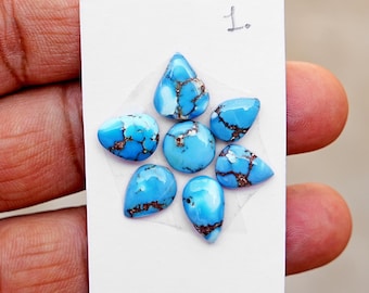 May include: A collection of six polished turquoise gemstones arranged on a white card labelled with the number 1. The stones feature a vibrant sky-blue colour with intricate, dark brown matrix webbing patterns, including one round and five teardrop shapes.