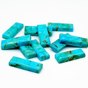 May include: A collection of rectangular turquoise gemstones with a polished finish. The stones vary in shades of blue and green, with brown veining. The gemstones are arranged on a white surface.