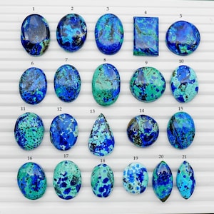 Peut inclure: Une collection de vingt-et-une pierres précieuses d'azurite polies de formes variées, dont des ovales, des cercles et un rectangle. Les pierres présentent un mélange de couleurs bleu profond et sarcelle avec des motifs uniques. Les pierres sont disposées sur une surface blanche.