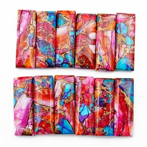May include: A collection of rectangular gemstone beads with a vibrant mix of colors. The beads feature a blend of pink, red, orange, and turquoise hues, accented with gold veining. The gemstones are arranged in two rows on a white background.