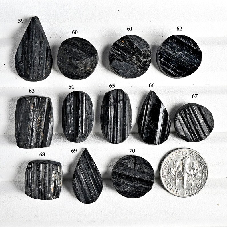 May include: A collection of black tourmaline gemstones in various shapes, including teardrop, oval, and round. The gemstones are polished and display natural striations. A US dime is included for size comparison.